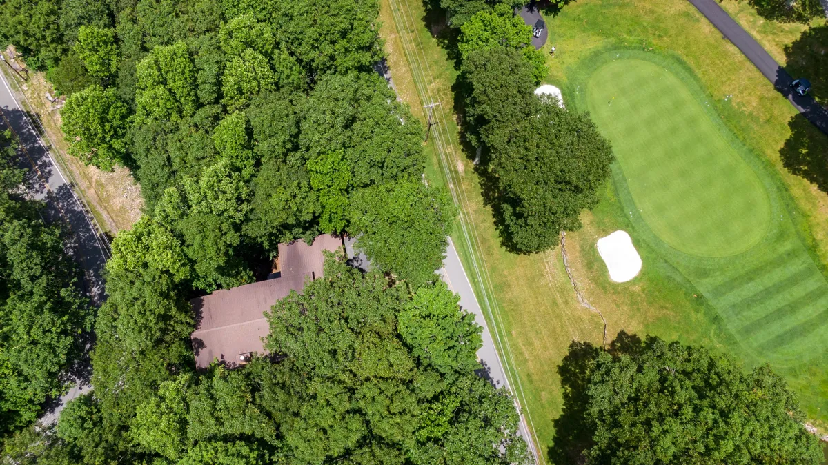 A view showing the golf course, surrounding roadway, house roof, and abundant greenery. The setting feels integrated—showing the proximity of homes to club amenities and the seamless transition from private space to the recreational outdoors.