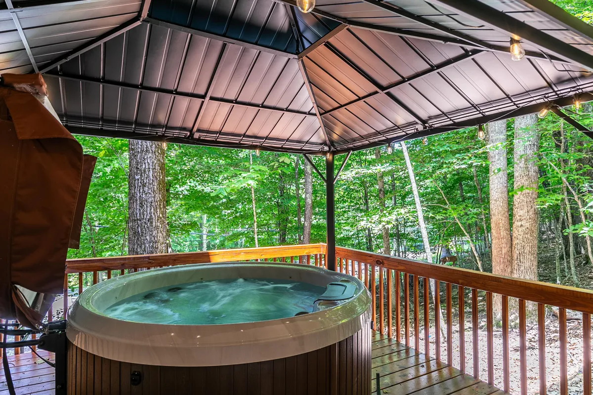 A serene view of a wooden deck nestled among trees, featuring a bubbling hot tub. The scene invites guests to unwind with nature, whether for group relaxation or quiet conversation.