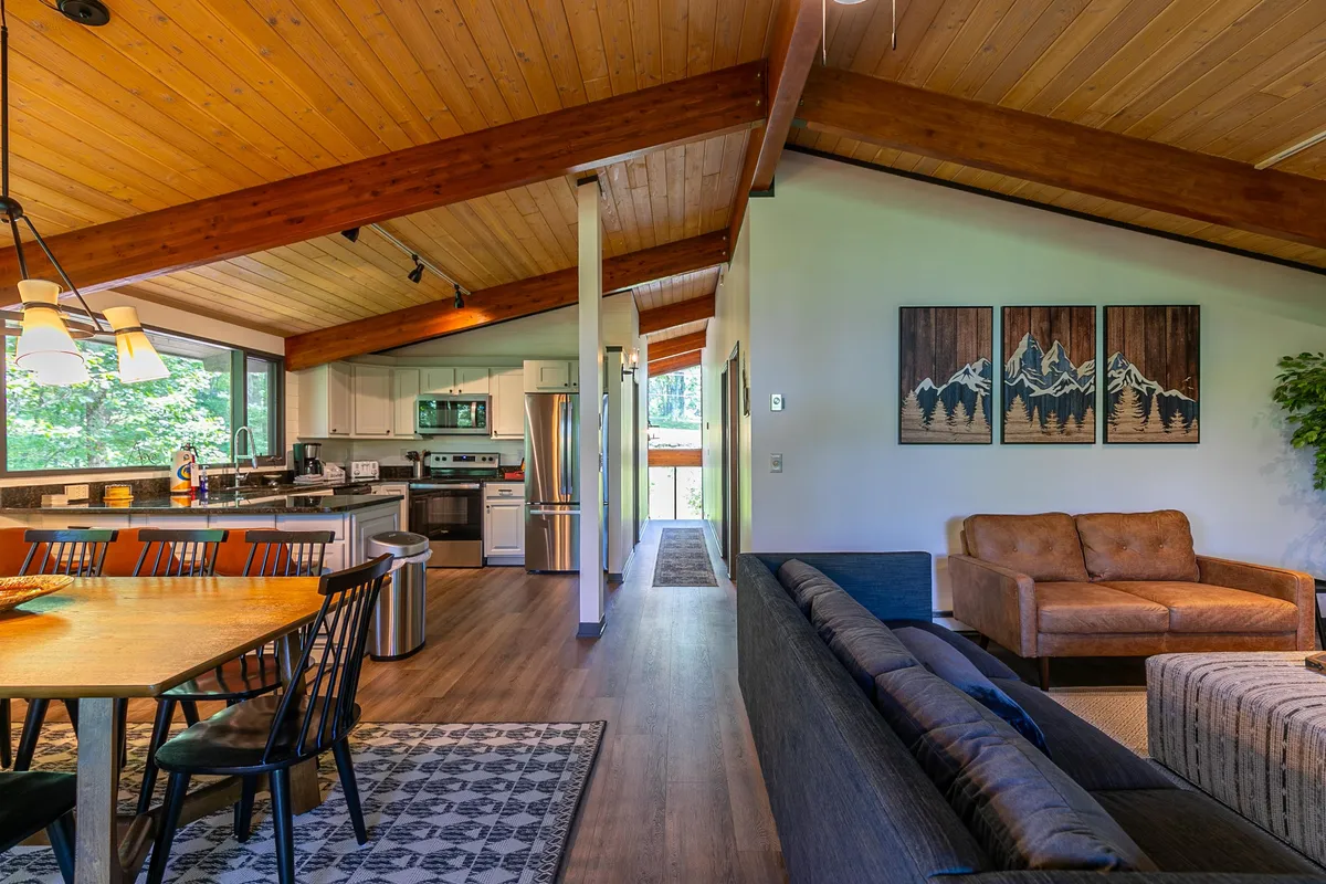 A welcoming perspective that encompasses the dining table, kitchen area, and living room seating, all arranged for socializing. Warmth from natural light and inviting decor create a sense of togetherness, perfect for family meals or game nights.