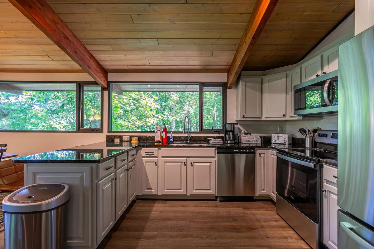 A cozy, modern kitchen featuring a central island with bar seating, large windows that let in natural light, and sleek stainless steel appliances. The open layout provides ample space for meal prep and socializing, with clear sightlines throughout the kitchen.