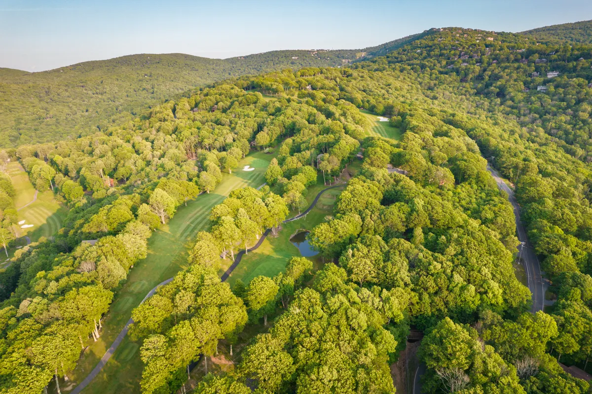 A scenic, wide-angle view of lush green trees, manicured golf course fairways, winding walking paths, and small ponds dotted across the landscape. The environment feels open, inviting, and perfect for outdoor recreation, with ample space for a variety of family adventures.