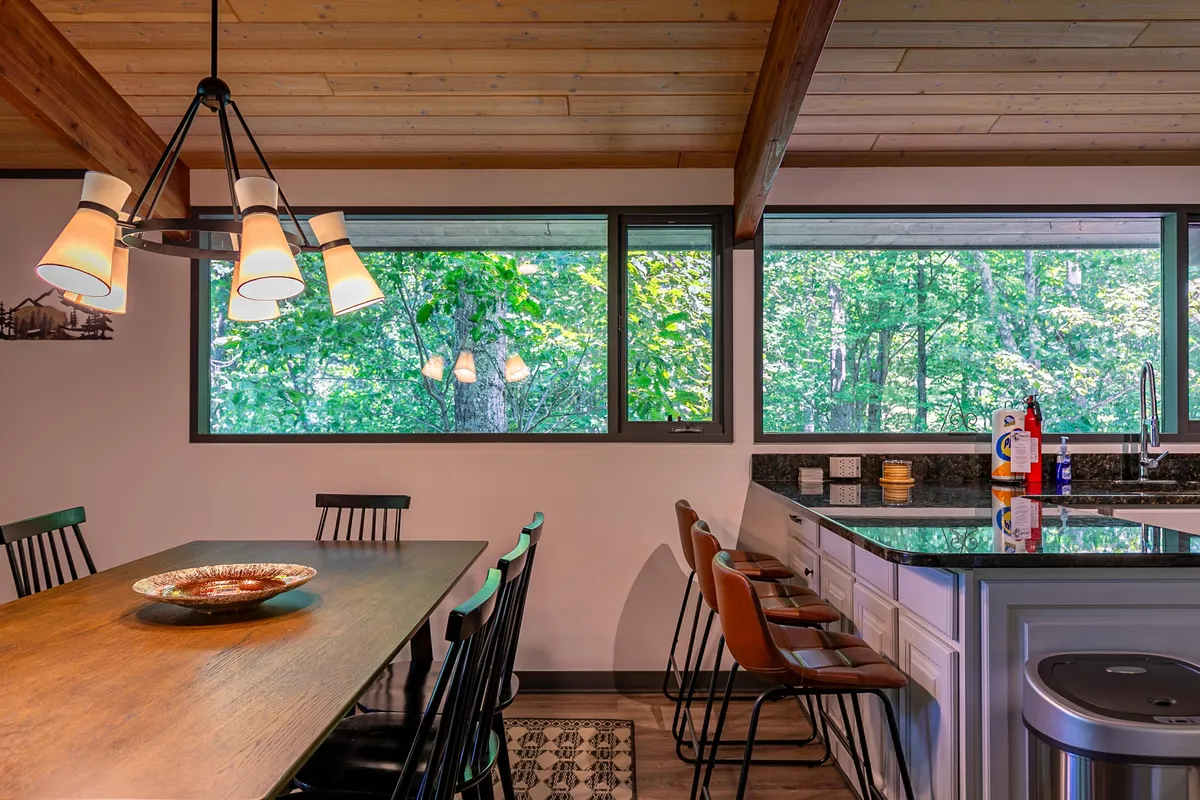 A bright, open-concept dining and kitchen space with a central island and a large table set near expansive windows. The setup encourages both cooking and dining together, with easy-to-clean surfaces and natural light creating a fresh, inviting atmosphere.