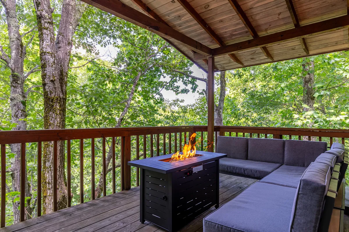 A cozy exterior scene with a fire pit surrounded by outdoor seating, set among tall trees. The setup invites socializing and unwinding after a day on the trails, with a natural backdrop that underscores the mountain chalet environment.