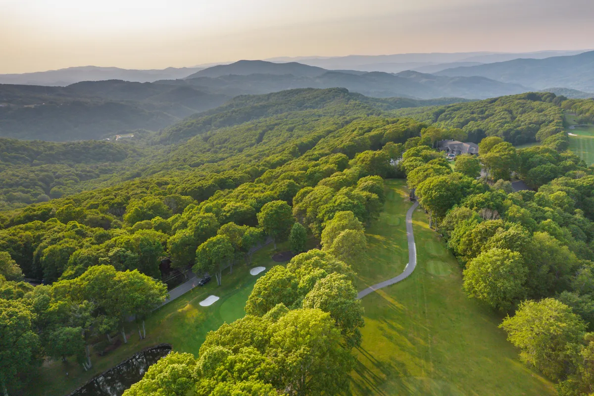 A scenic view over a lush green golf course framed by rolling hills, winding paths, and clusters of trees. The landscape is inviting for activities like golfing, hiking, and leisurely family outings, and the open sky hints at beautiful sunsets.